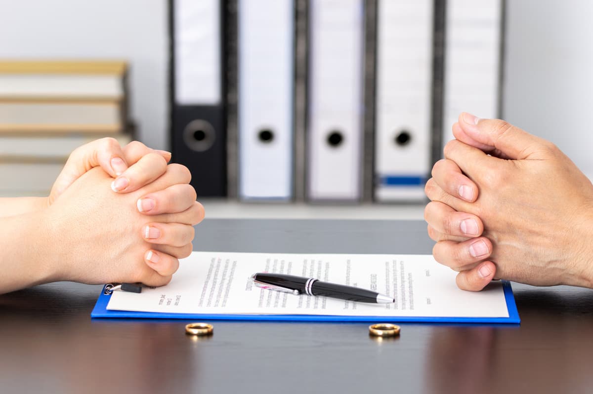 Manos sobre un acuerdo de divorcio con anillos sobre la mesa
